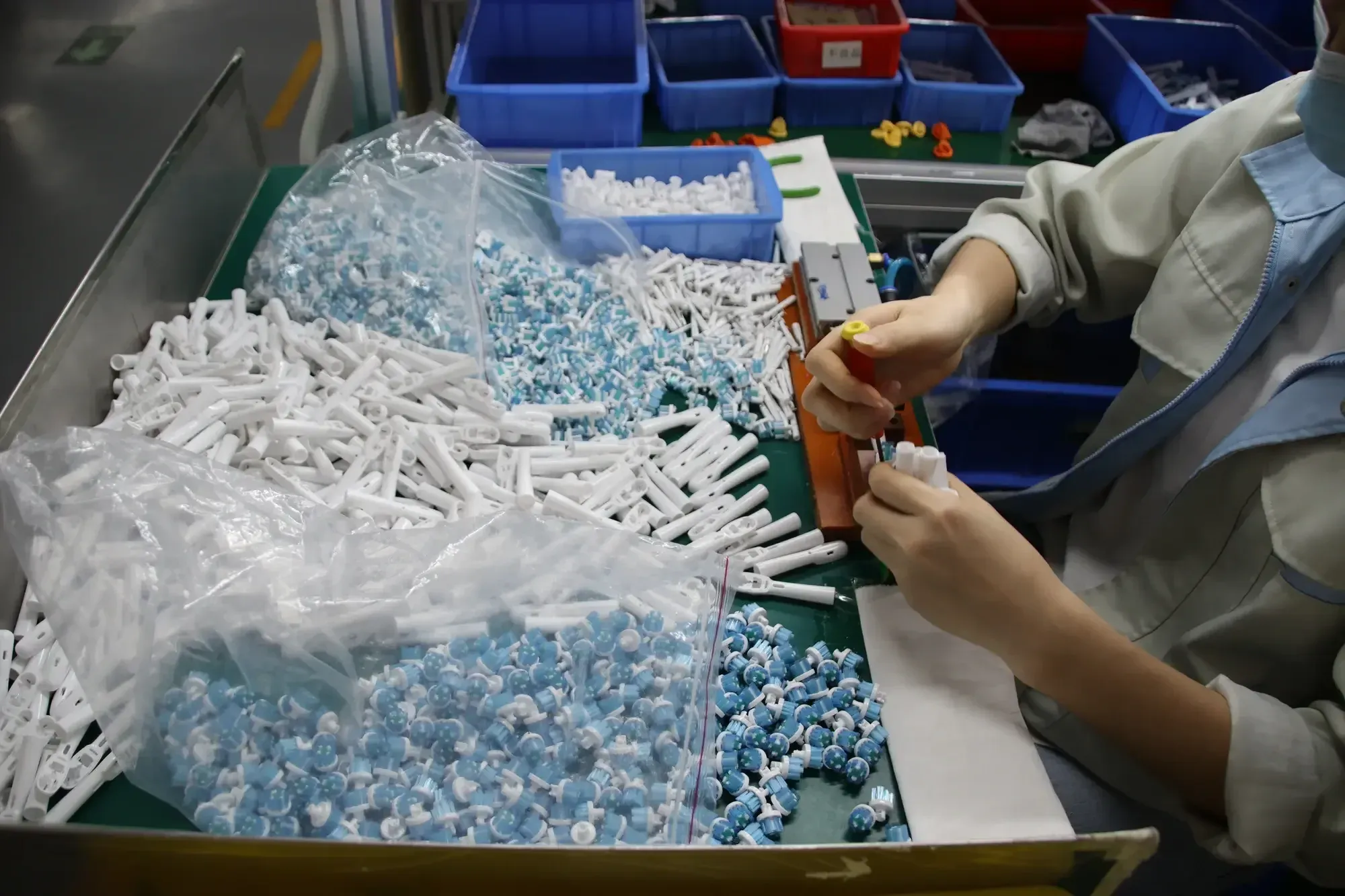 Worker assembling small electric toothbrush brush head components at an AileCare workbench